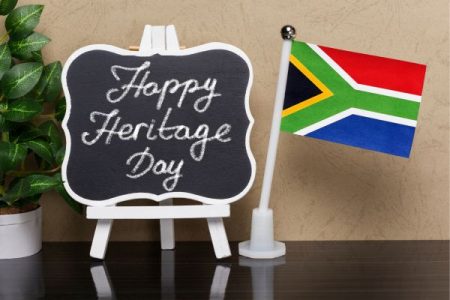 Small sign on small easel painted white next to small south african flag. the sign reads Happy Heritage Day