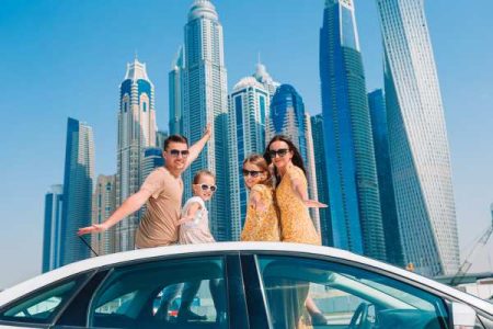 Family posing on a car in front of the Dubai Skyline in a blog about family travel that includes a section about travel to the middle east