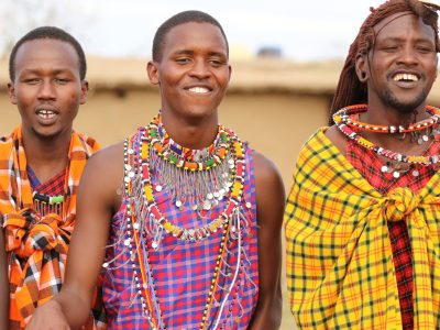 Masaai villagers in Kenya wearing colourful clothing and beads on the occasion of tourists visiting their homes. This image is being used to illustrate a section of a blog article discussing how responsible travel can protect lands, animals and communities.
