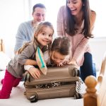 Family on a bed packing a suitcase which is overflowing and the children are trying to foce it closed as Mum helps and Dad looks on. Used in a blog with a list of 10 tips to help with planning a family holiday