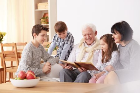 A family group spanning three generations with grandparents and children looking through a photo album to illustrate that family vacations are a great way to make long lasting memories