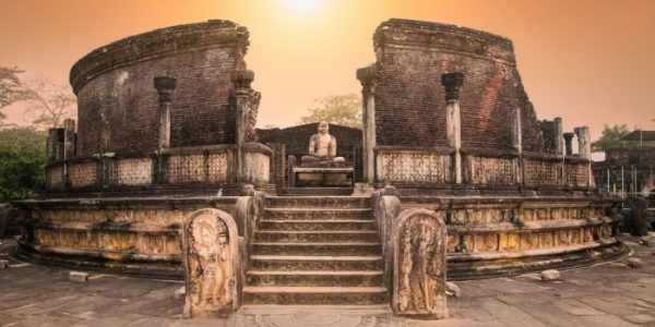 Ancient stone ruins of the Polonnaruwa Vatadage in Sri Lanka, featuring intricately carved guardstones, a stairway with ornate detailing, and a seated Buddha statue at the center under a bright blue sky. This UNESCO World Heritage Site showcases the island’s remarkable heritage and ancient Buddhist architecture.