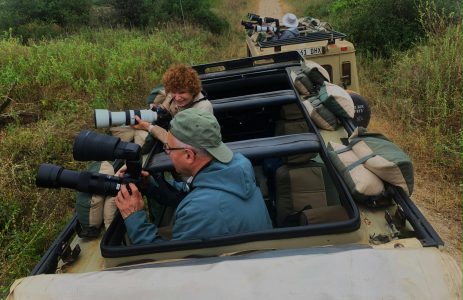 Photographers with professional gear and lenses in a safari vehicle.