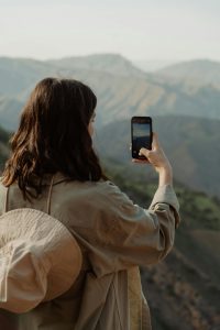 Photo of a woman using a smartphone to take a photograph of landscapes.